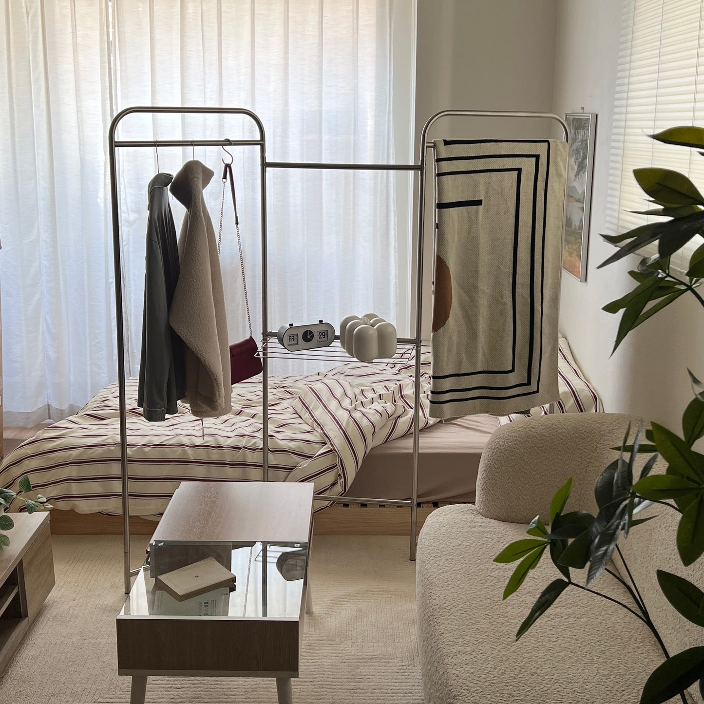 フォールディング式のパーテーションハンガーラックにブランケットをかけてベッドとリビングの間を間仕切りしている部屋