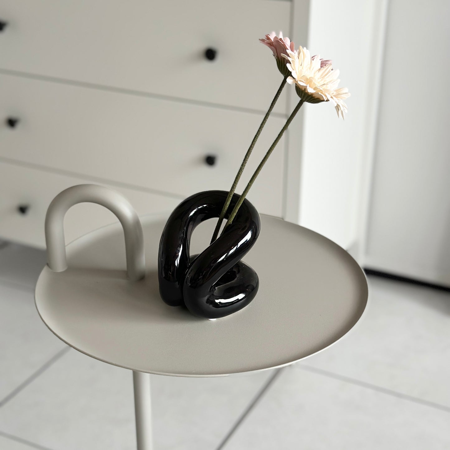 丸テーブルの上に花が2本飾られたセラミックの黒のオブジェが置かれている