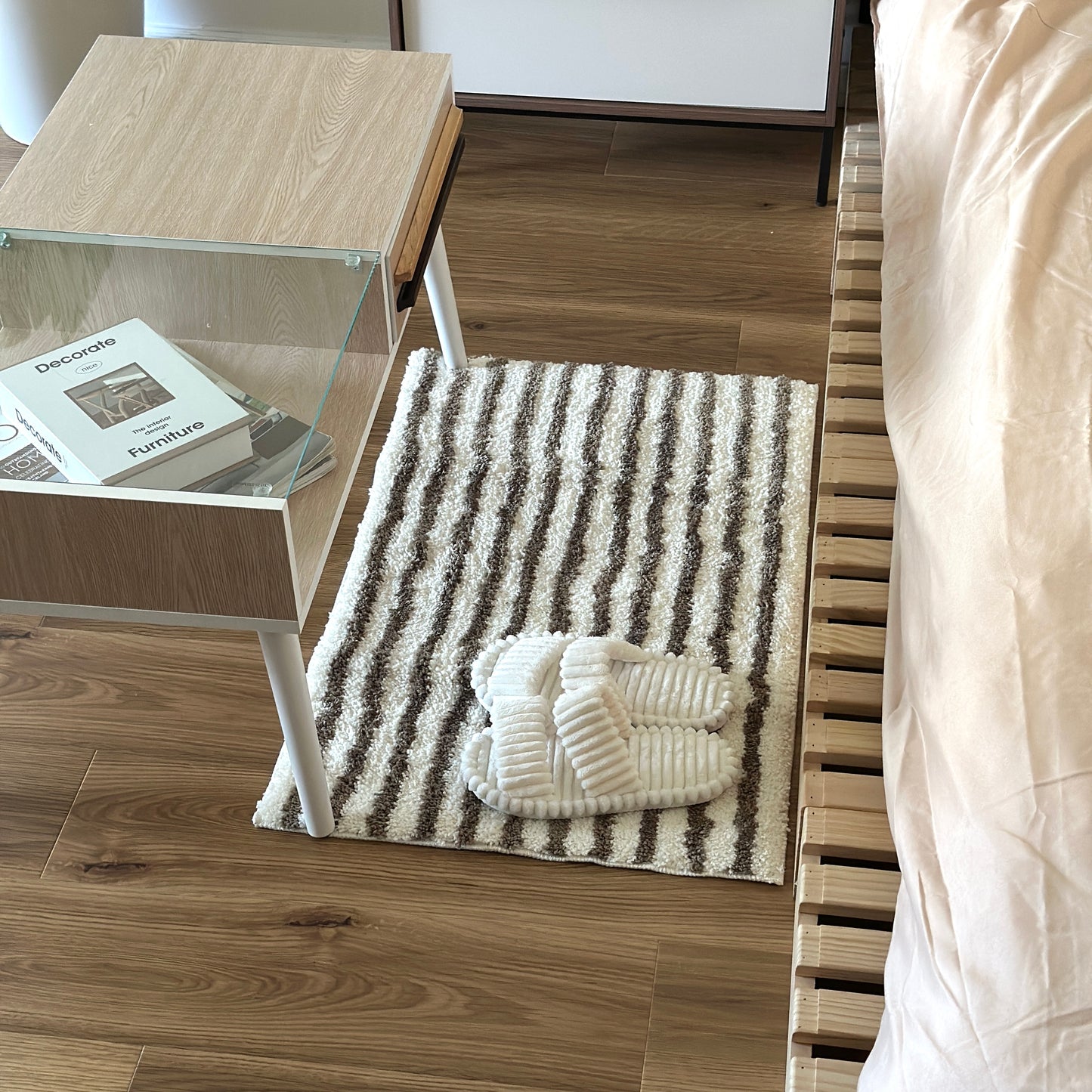 カーキのシンプルなボーダーミニラグをベッド横に敷いている様子