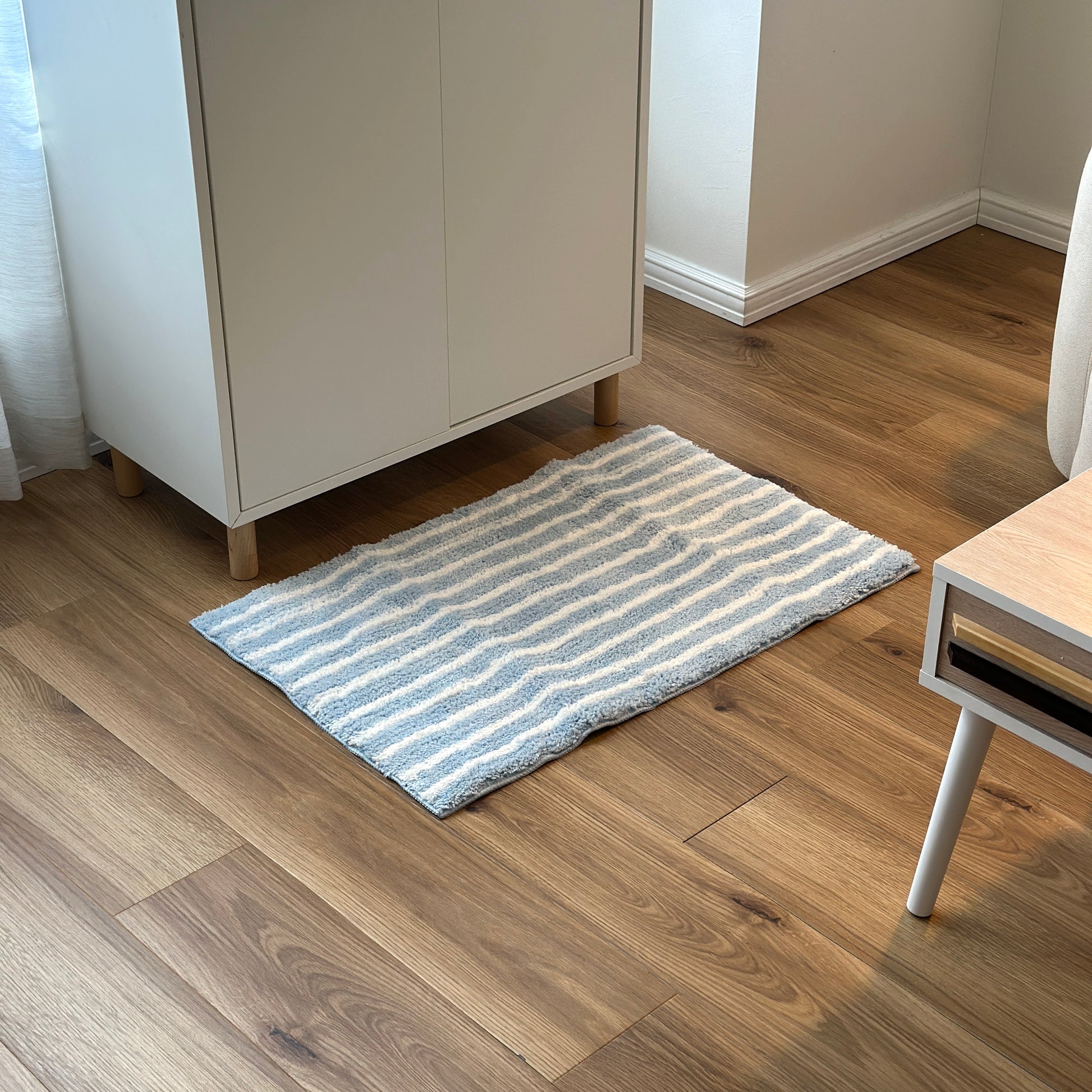 ライトブルーのシンプルなボーダーミニラグを白棚の前に敷いている様子