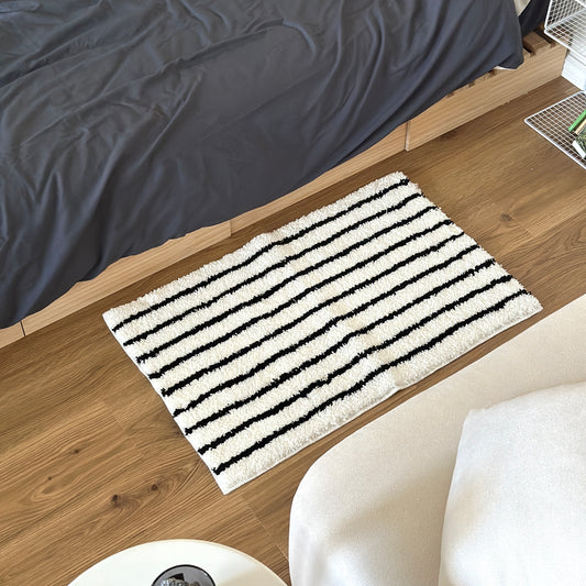 ブラックのシンプルなボーダーミニラグをベッド横に敷いている様子