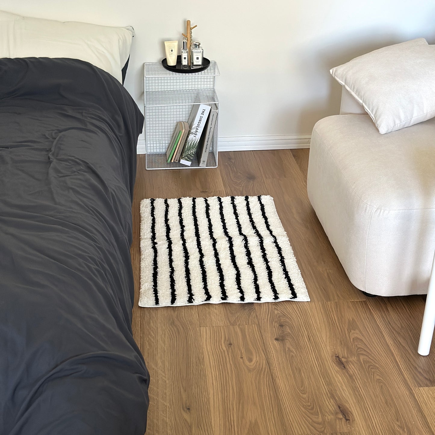 ブラックのシンプルなボーダーミニラグをベッド横に敷いている様子
