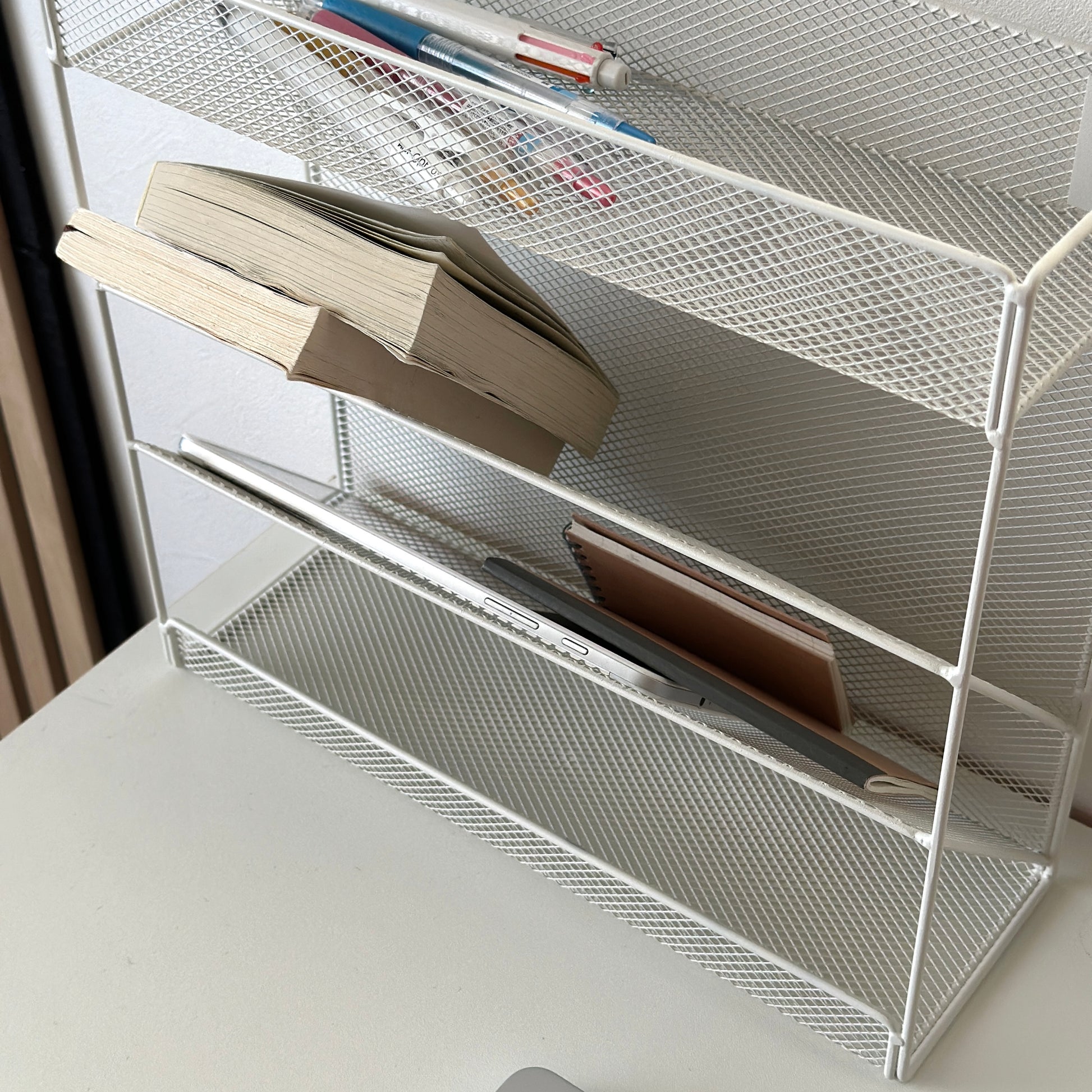 ホワイトのメッシュデザインの4段構造ラックにペンや文庫本などを置いている様子