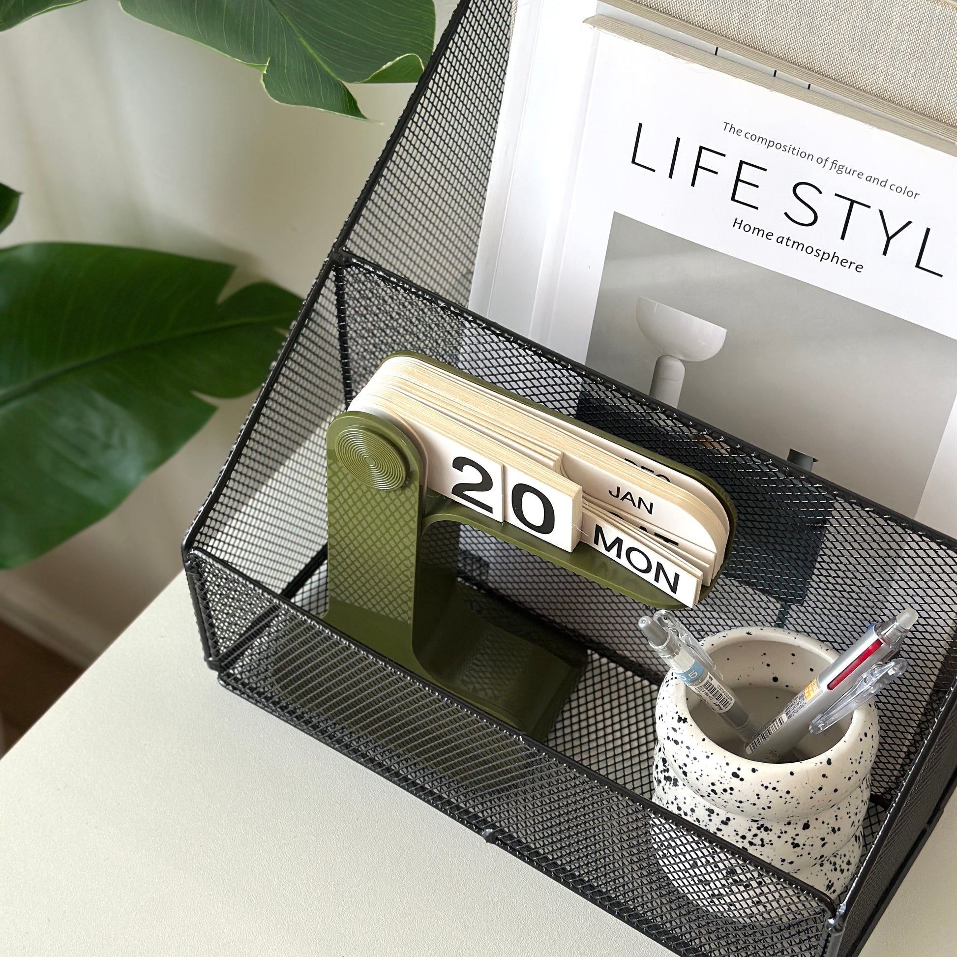 ブラックのアイアン素材のメッシュ収納ラックに雑誌や卓上カレンダー、ペンが入っている様子