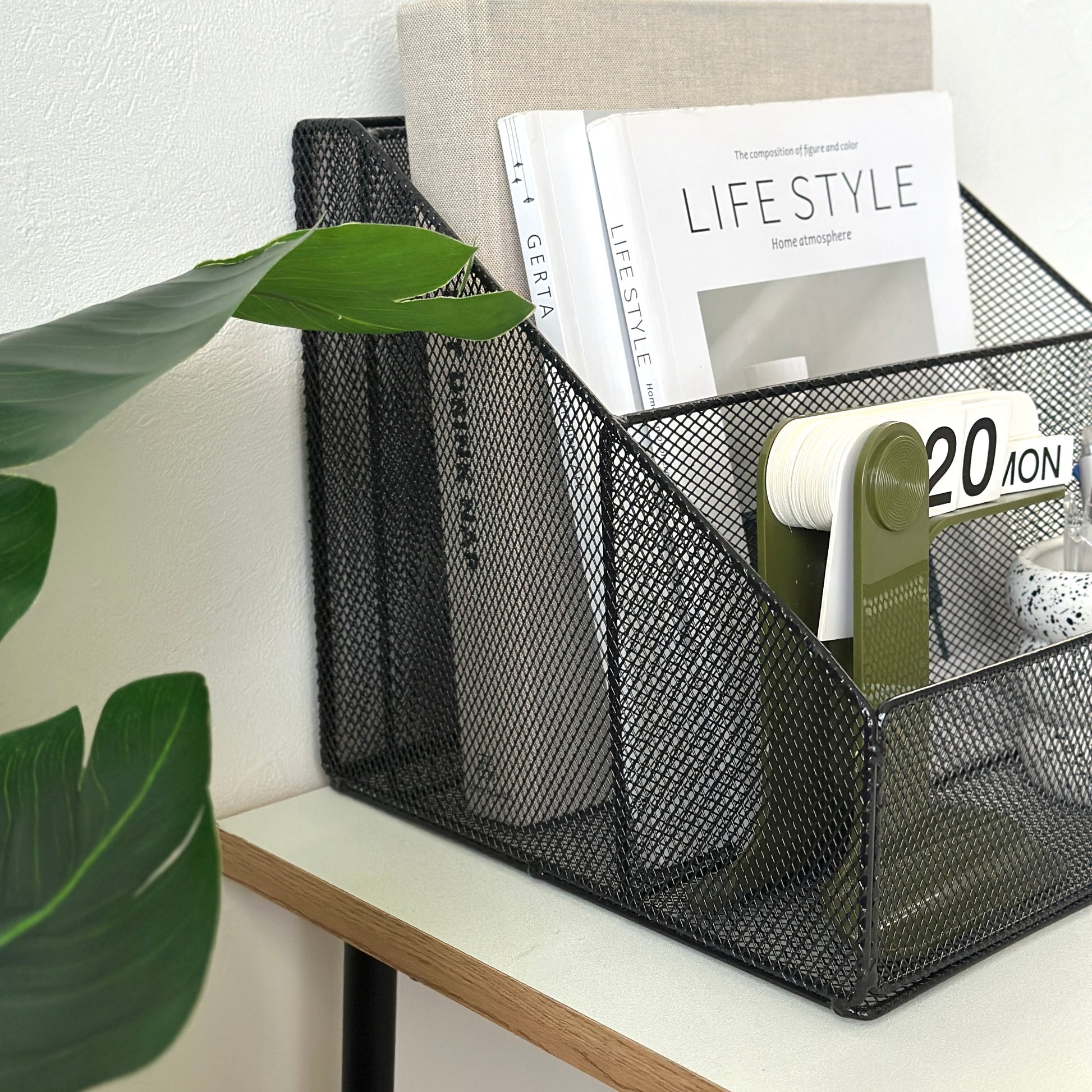 ブラックのアイアン素材のメッシュ収納ラックに雑誌や卓上カレンダー、ペンを入れている様子