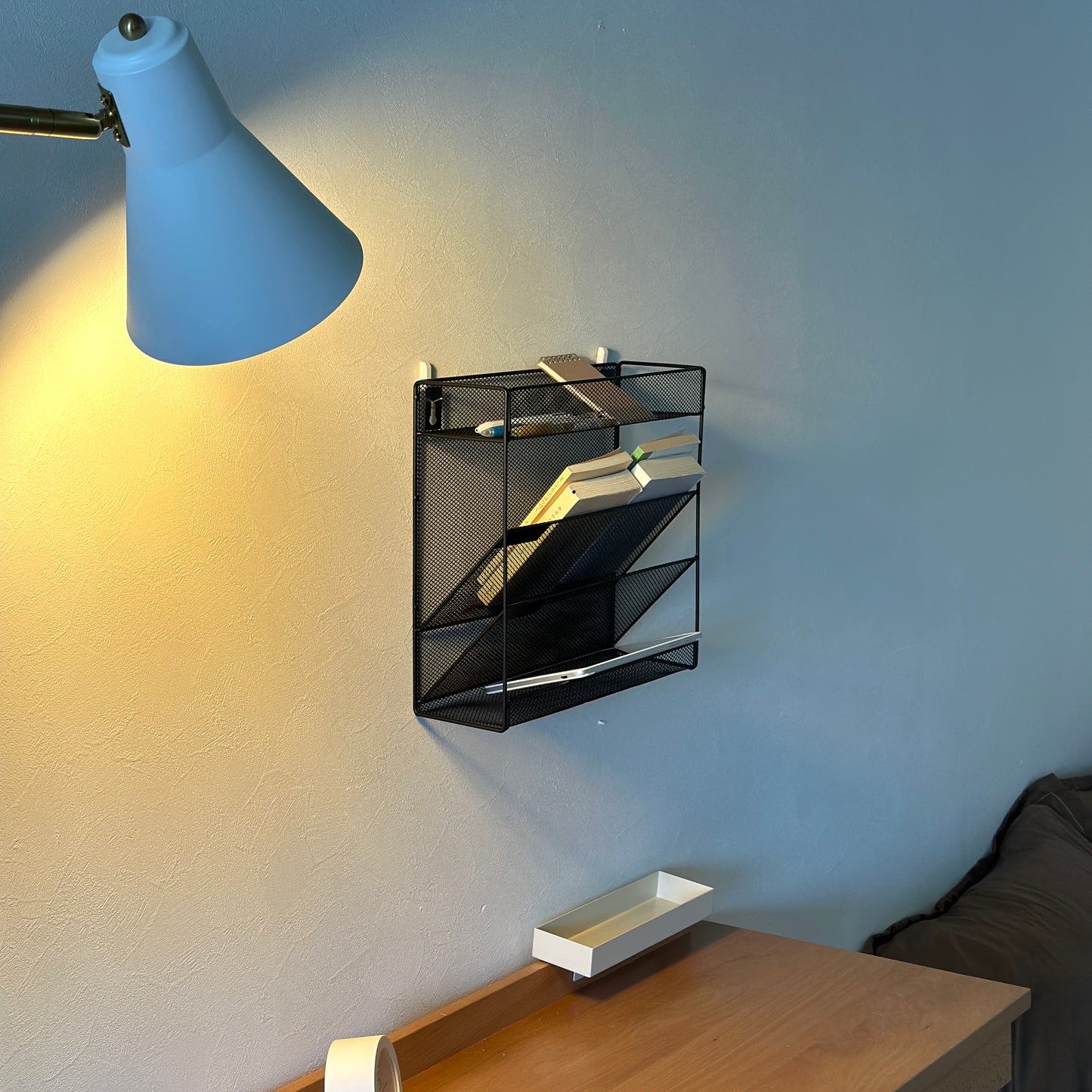 ブラックのメッシュデザインの4段構造ラックをデスク上の壁にかけている様子