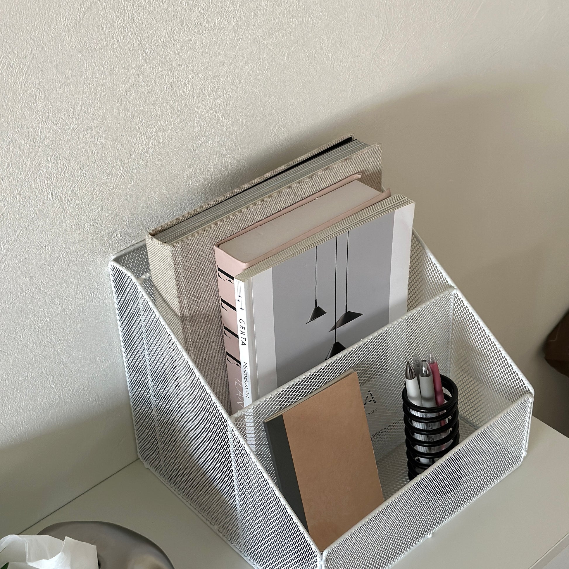 ホワイトのアイアン素材のメッシュ収納ラックに雑誌やメモ帳、ペンを入れている様子