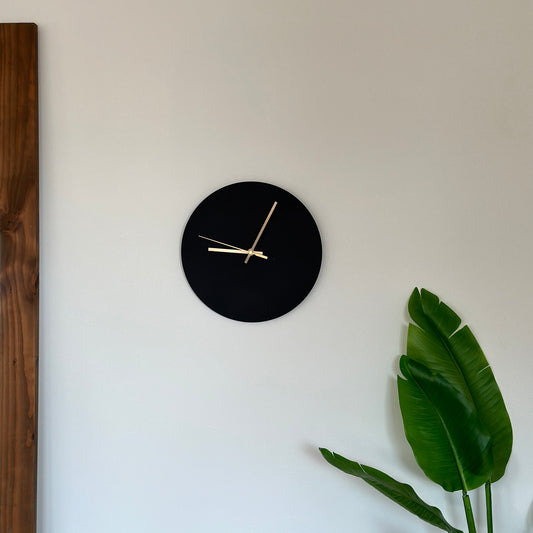 壁にかけられた本体がブラックで針がゴールドのシンプルな掛け時計