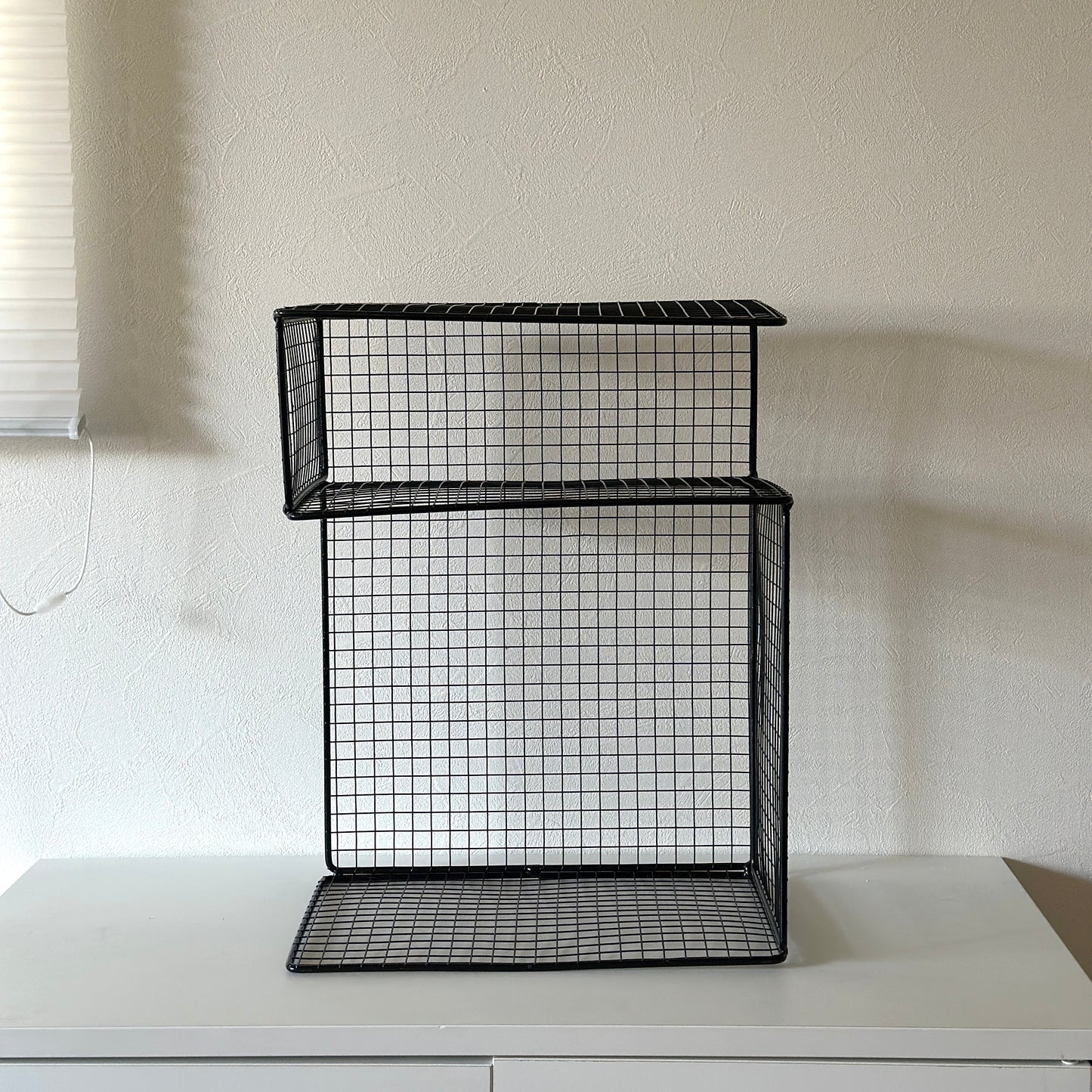 ブラックのメッシュデザインの収納ラックが白棚の上に置かれてある様子