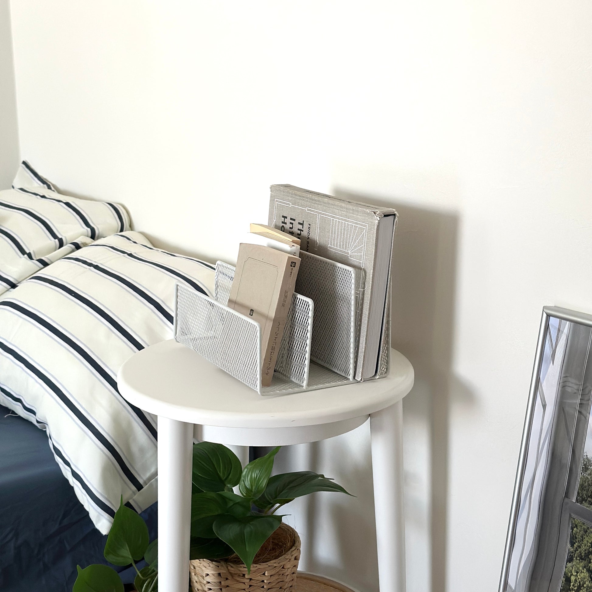 ホワイトのアイアン素材のマガジンラックをベッド横のサイドテーブルに置いている様子