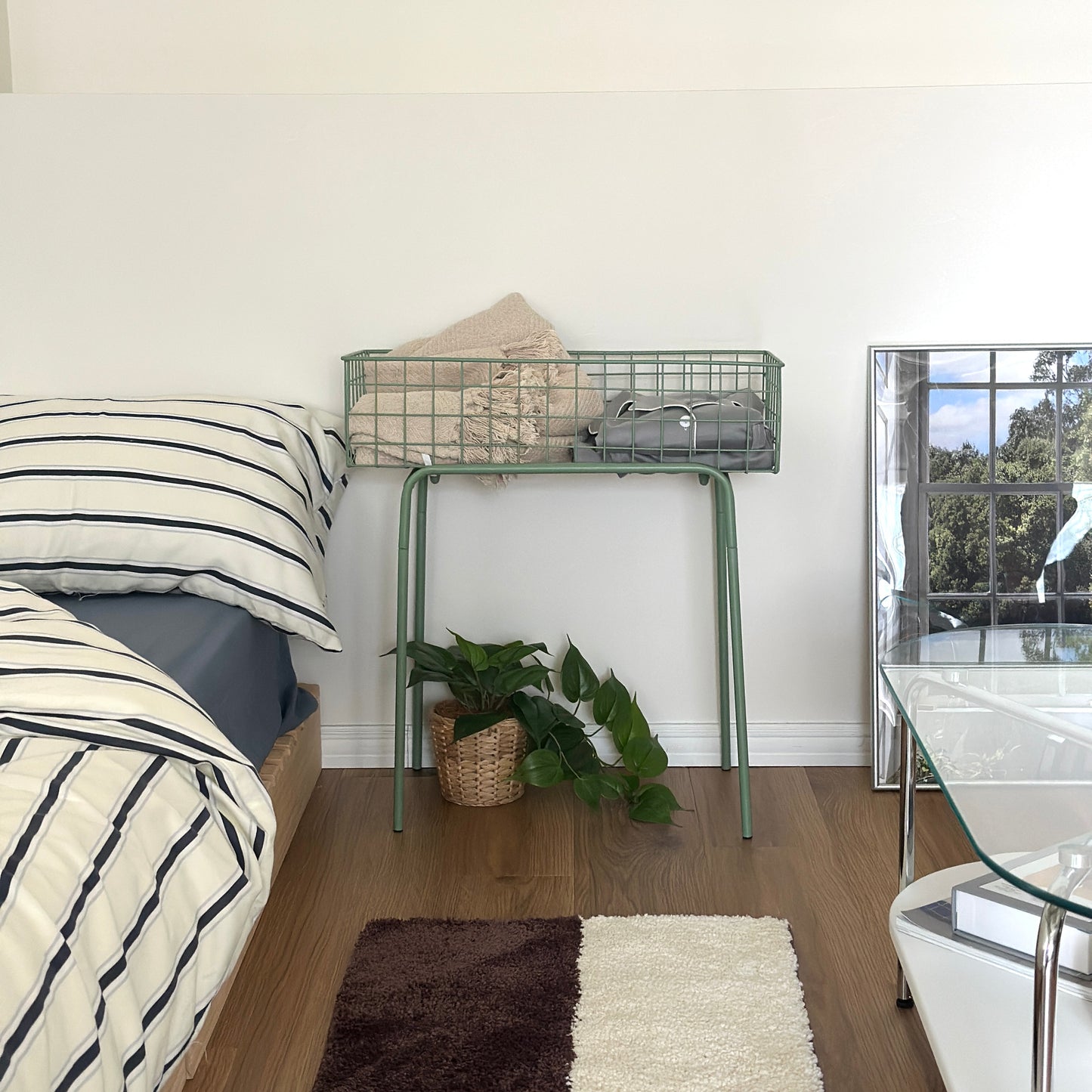 エメラルドのアイアン素材とワイヤーメッシュデザインの収納ワゴンをベッド横に置いている様子