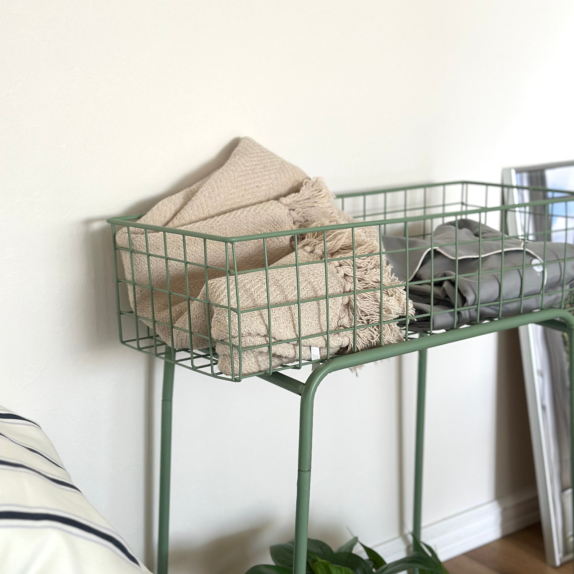 エメラルドのアイアン素材とワイヤーメッシュデザインの収納ワゴンにブランケットとパジャマを入れている様子