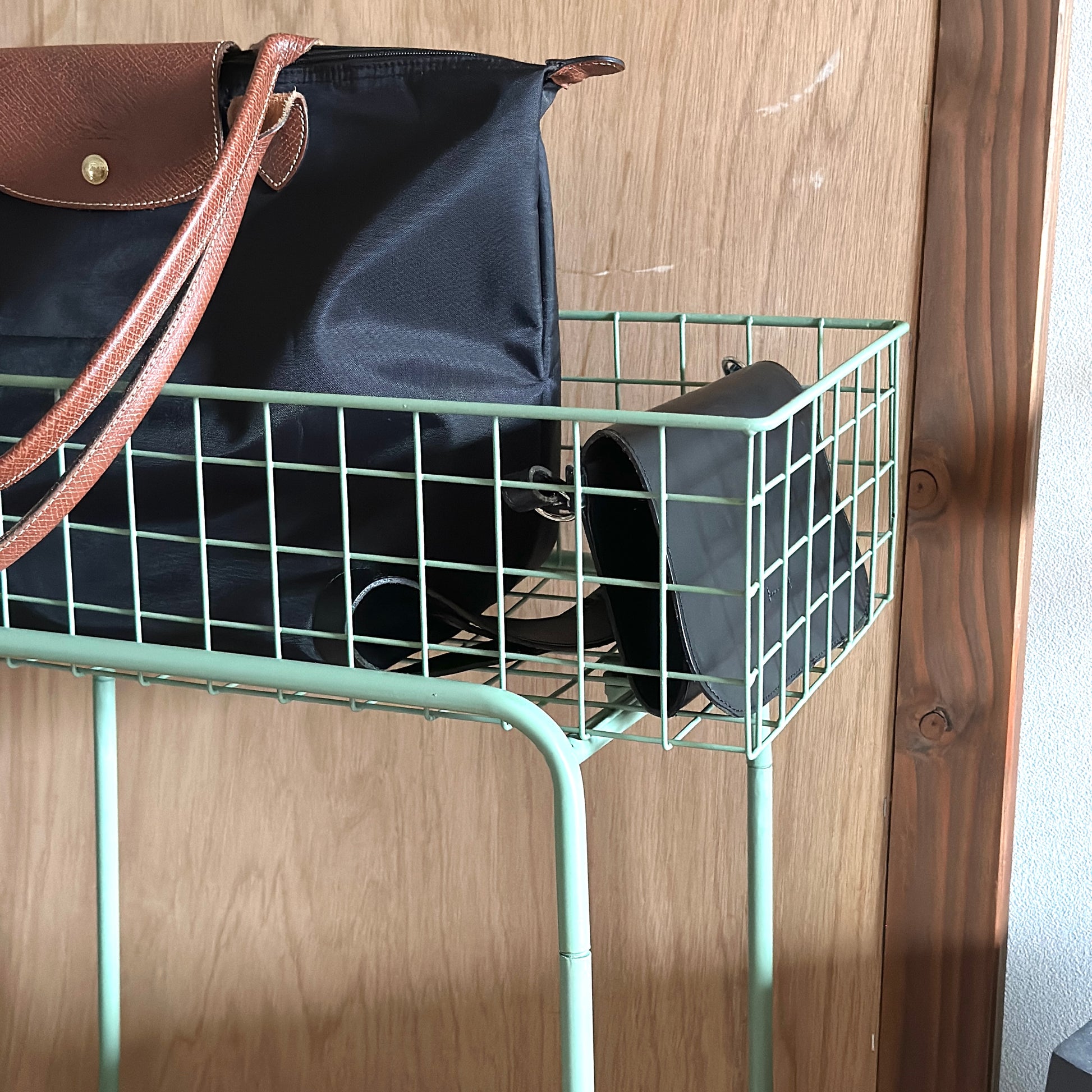 エメラルドのアイアン素材とワイヤーメッシュデザインの収納ワゴンにバッグを入れている様子