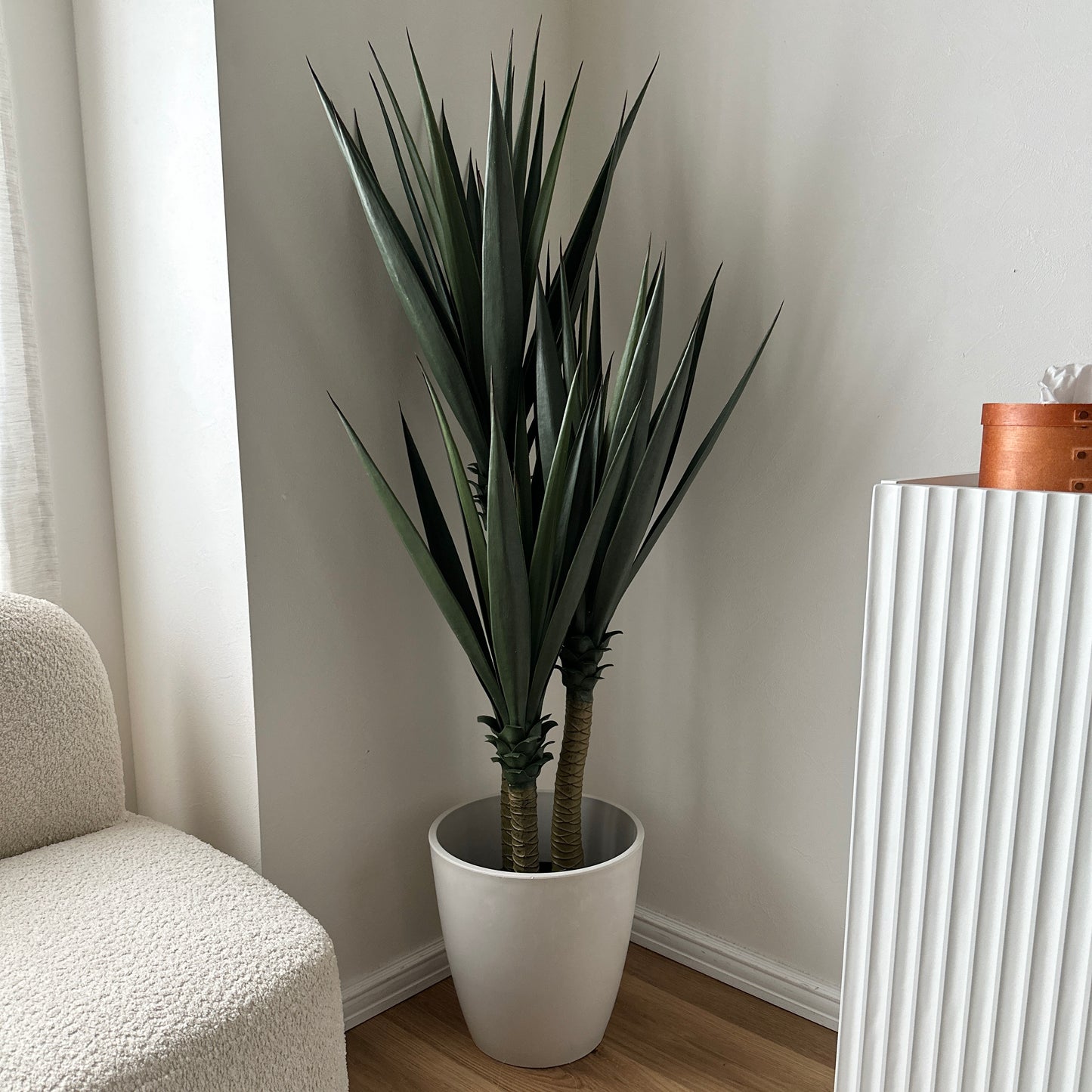 フェイクグリーンのユッカ植物、高くて濃い緑の長くてとげとげした葉が白い陶器鉢に入っています。