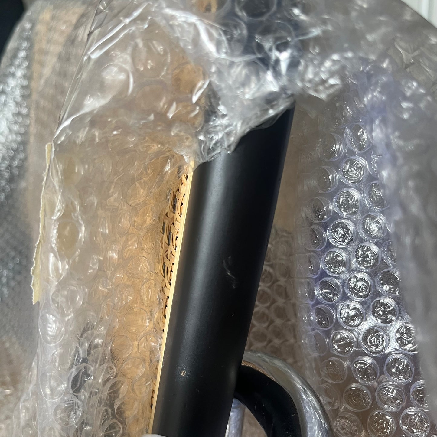 黒ラタンパイプチェアの肘掛け黒い円柱形ハンドルにテクスチャ付きの金色側面パネルがラップ包装されている画像