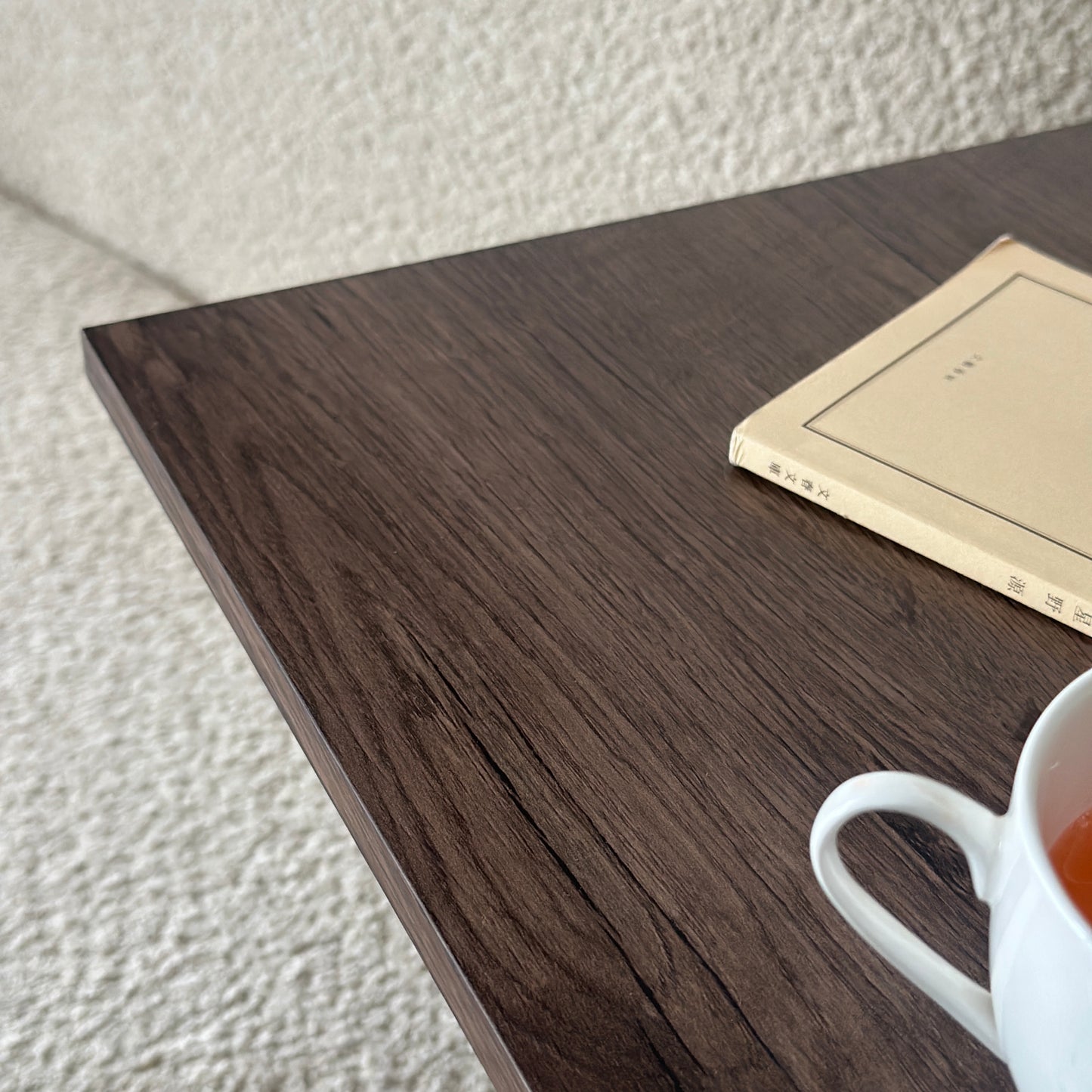 ブラウンの2way置きサイドテーブルに文庫本とコップを置いている様子