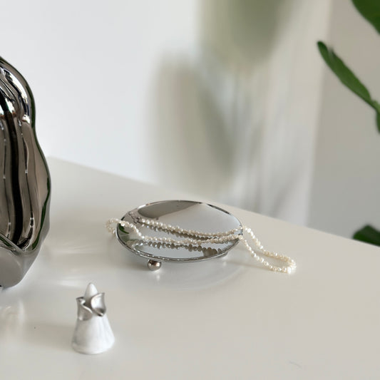 脚付のシルバーのステンレス製の丸いプレートにアクセサリーが置かれている