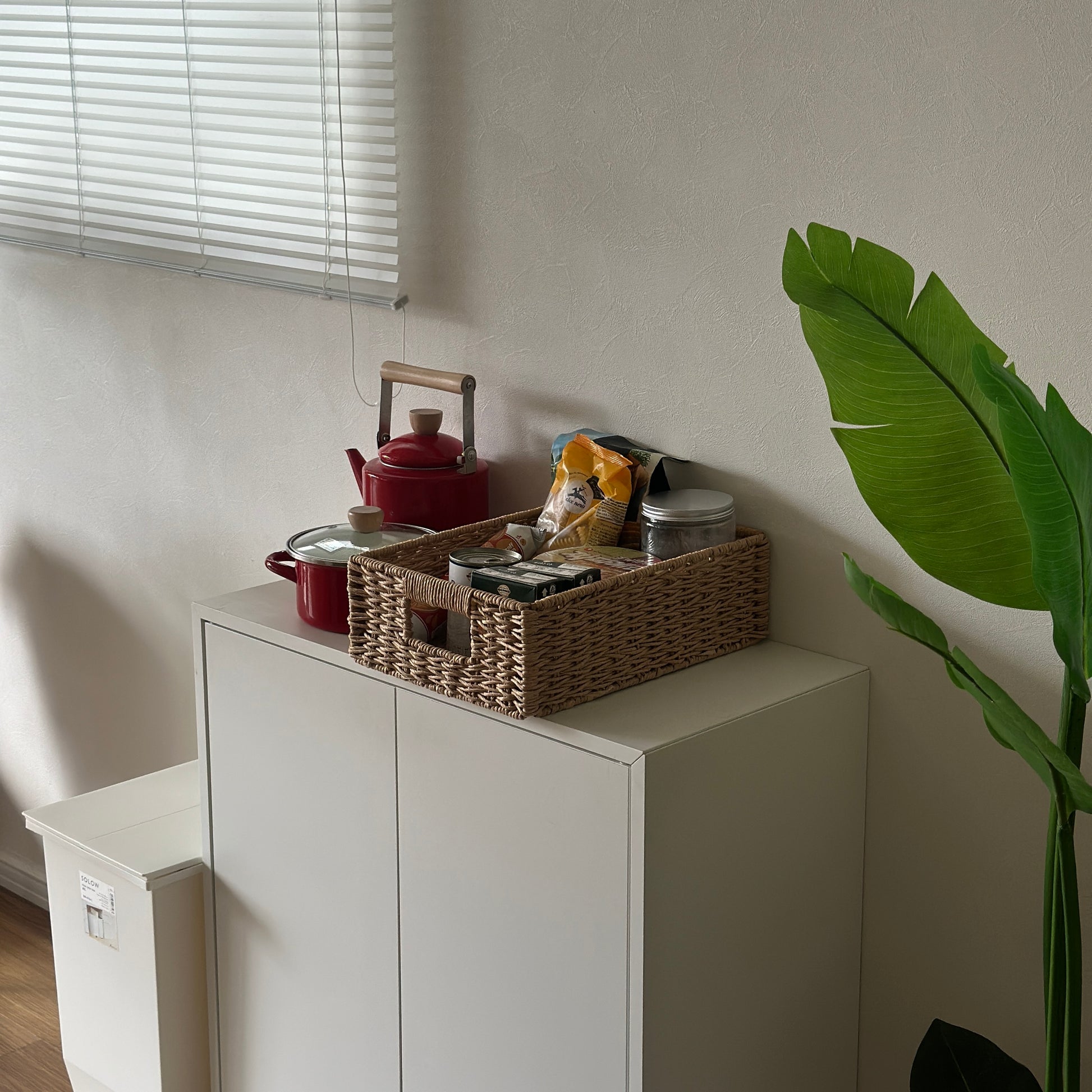 手編みの折り畳み式ペーパーコードバスケットの中に食料品を入れて白棚の上に置いている様子