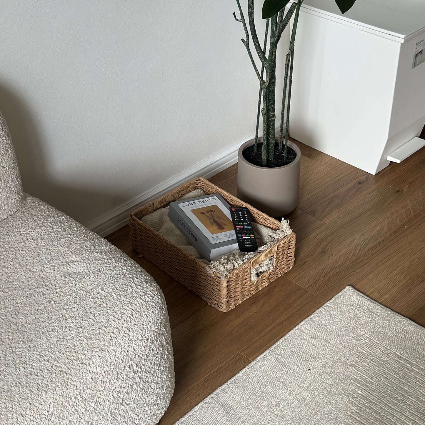 手編みの折り畳み式ペーパーコードバスケットの中にブランケットと本とリモコンが入っている様子