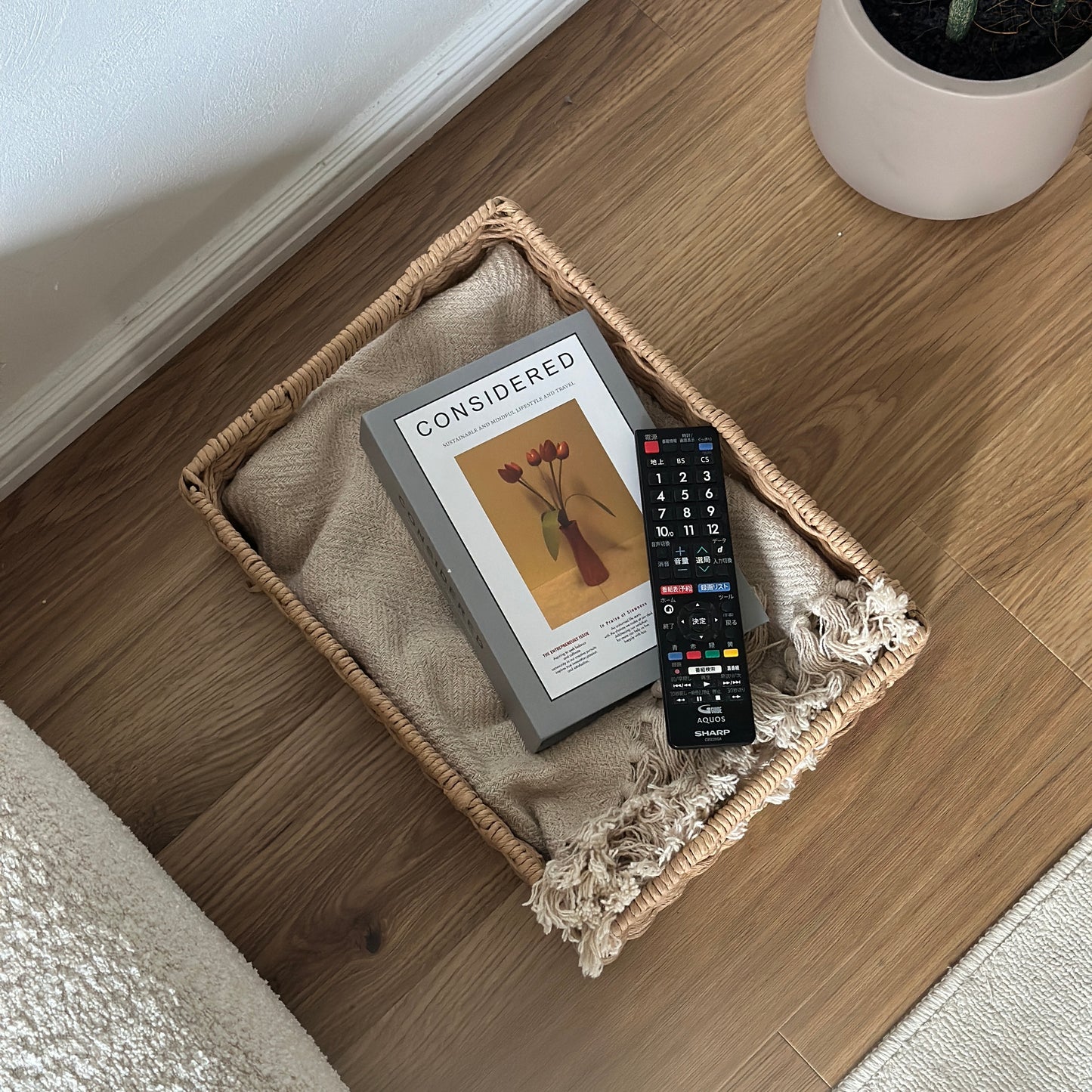手編みの折り畳み式ペーパーコードバスケットの中にブランケットと本とリモコンが入っている様子