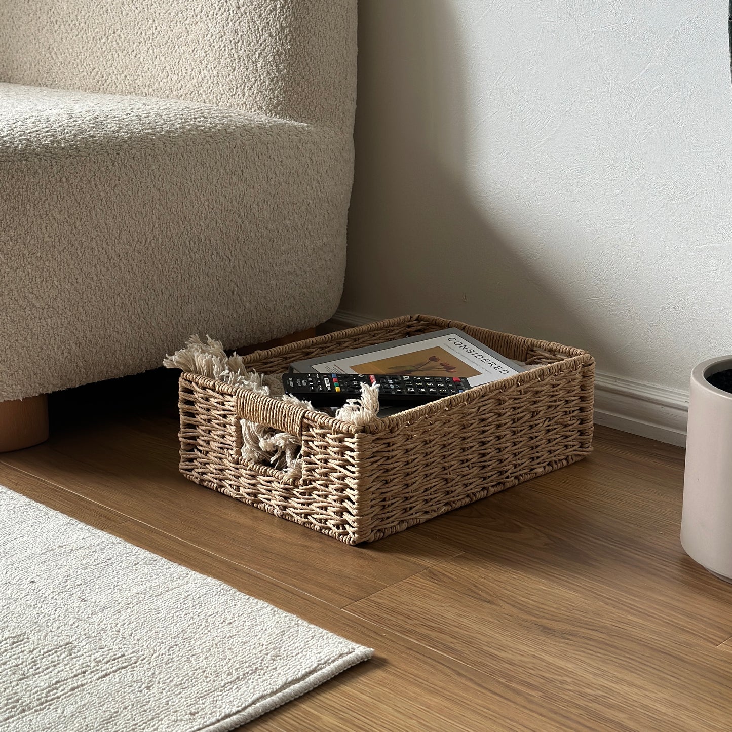 手編みの折り畳み式ペーパーコードバスケットの中にブランケットと本とリモコンが入っている様子