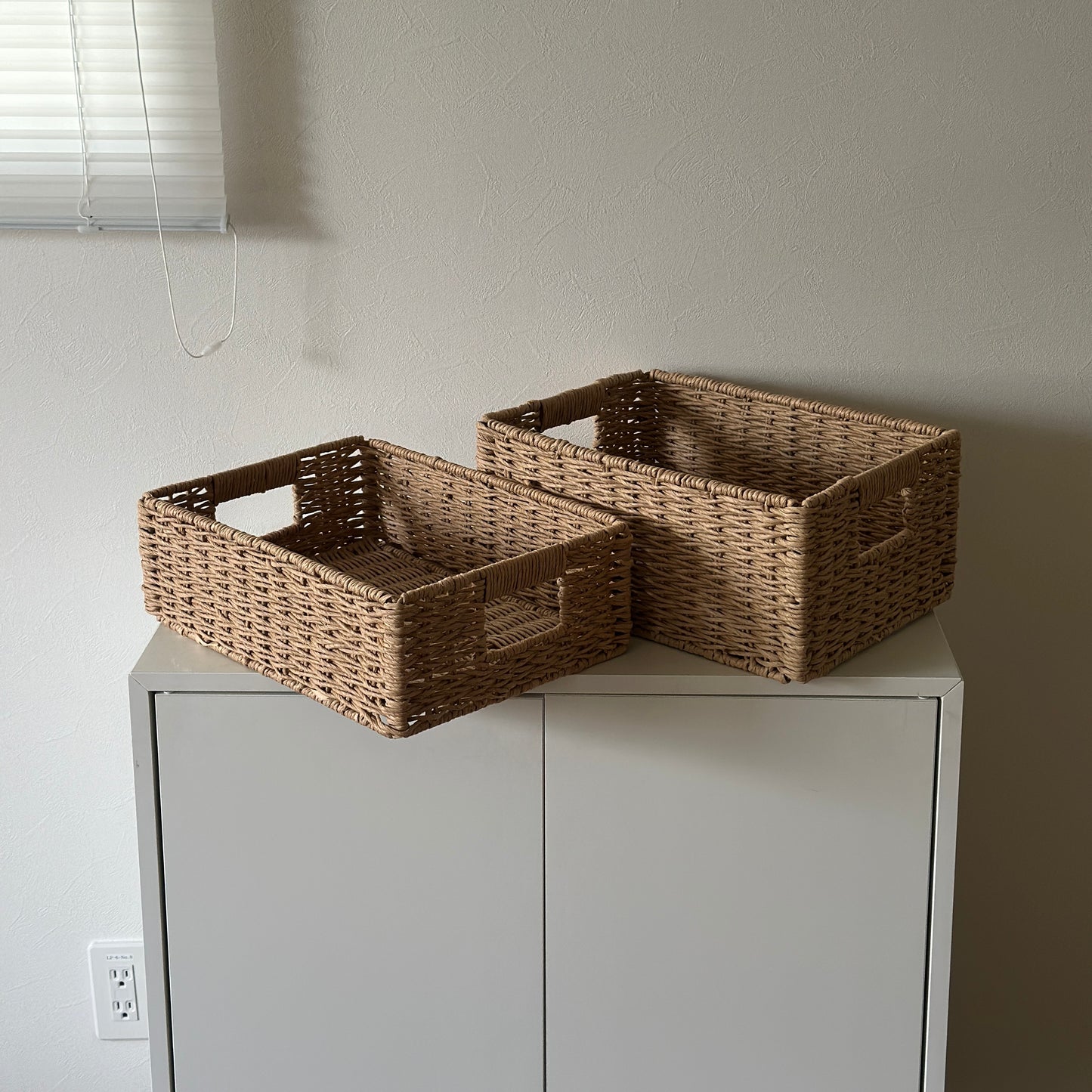 手編みの折り畳み式ペーパーコードバスケットのサイズ違いを白棚の上に並べている様子