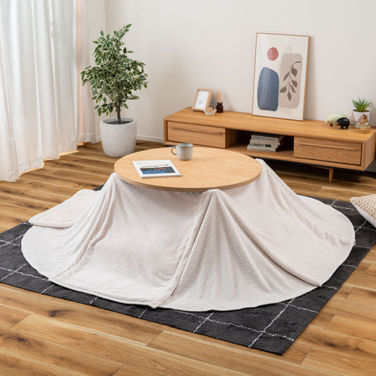 部屋の中心にナチュラルウッドな天板にアイボリーのこたつ布団が掛かったこたつが置いてる様子