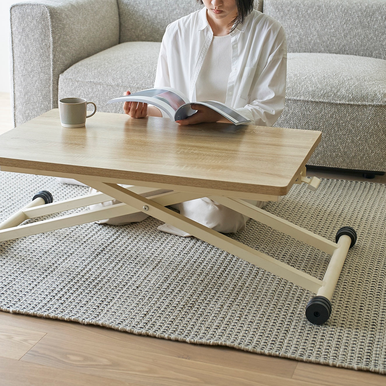 ナチュラルの高さ調節可能なテーブルをローテーブルとしてソファ前に置いている様子