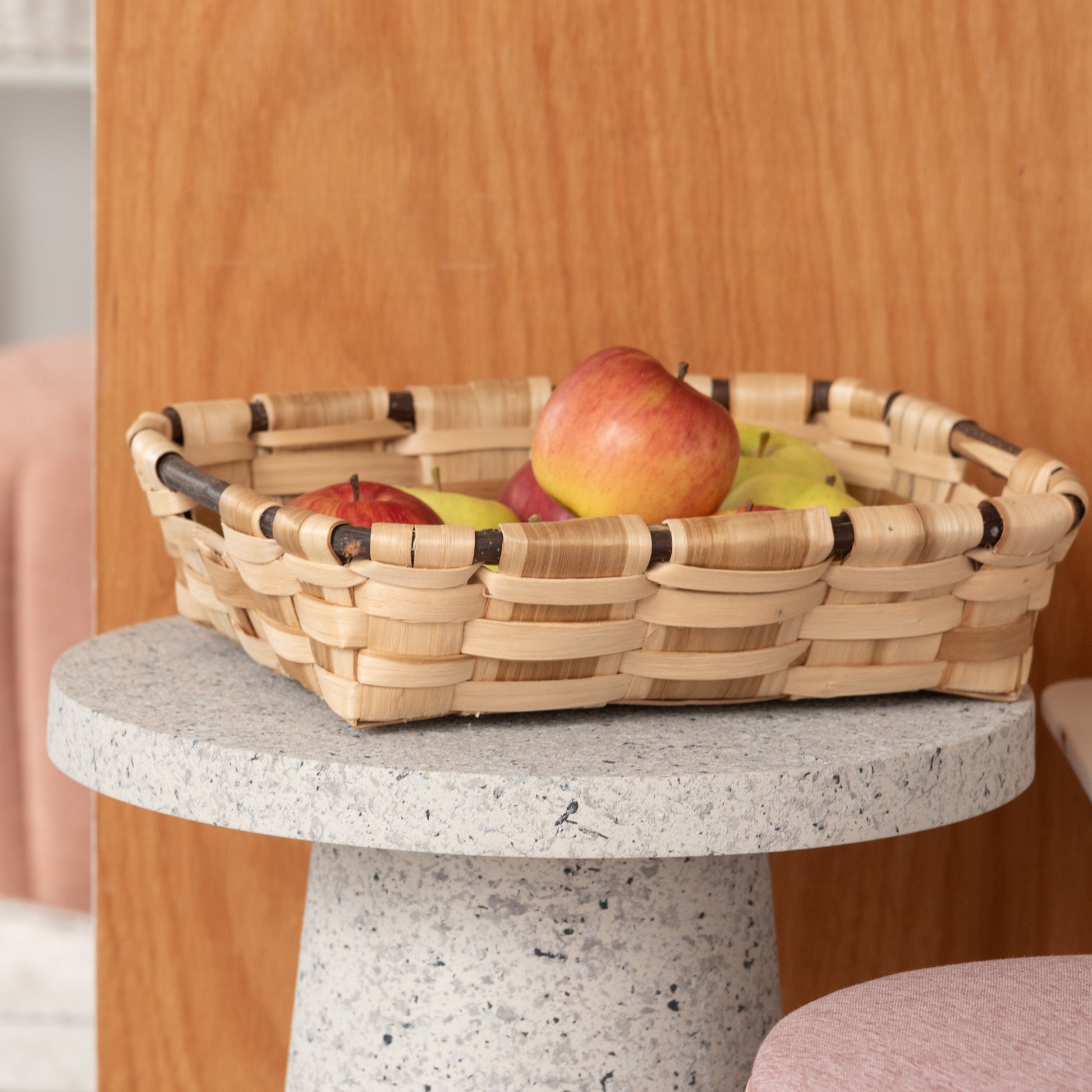 テラゾー柄ラウンドサイドテーブルの上にりんごの入ったバスケットが置いてある様子