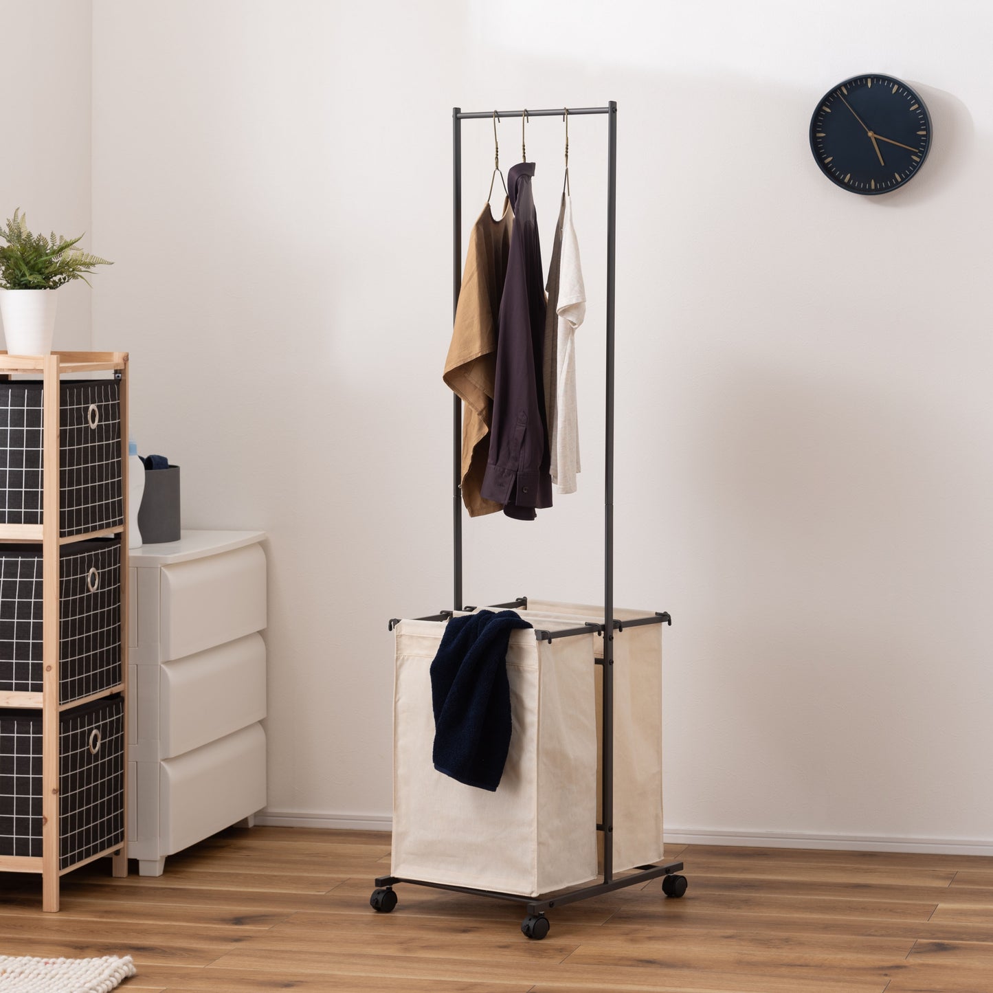 ダークグレーのスタイリッシュなスチールフレームの2つカゴ付きランドリーハンガーが部屋に置いてある写真