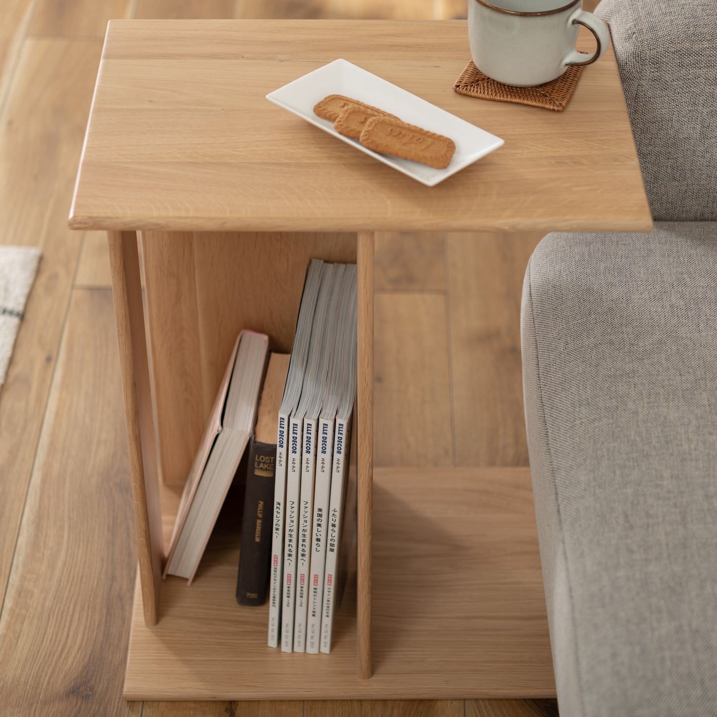 ラック付きオークサイドテーブルのラックに雑誌が収納されていて、天板にはお菓子とお茶が置いてある様子