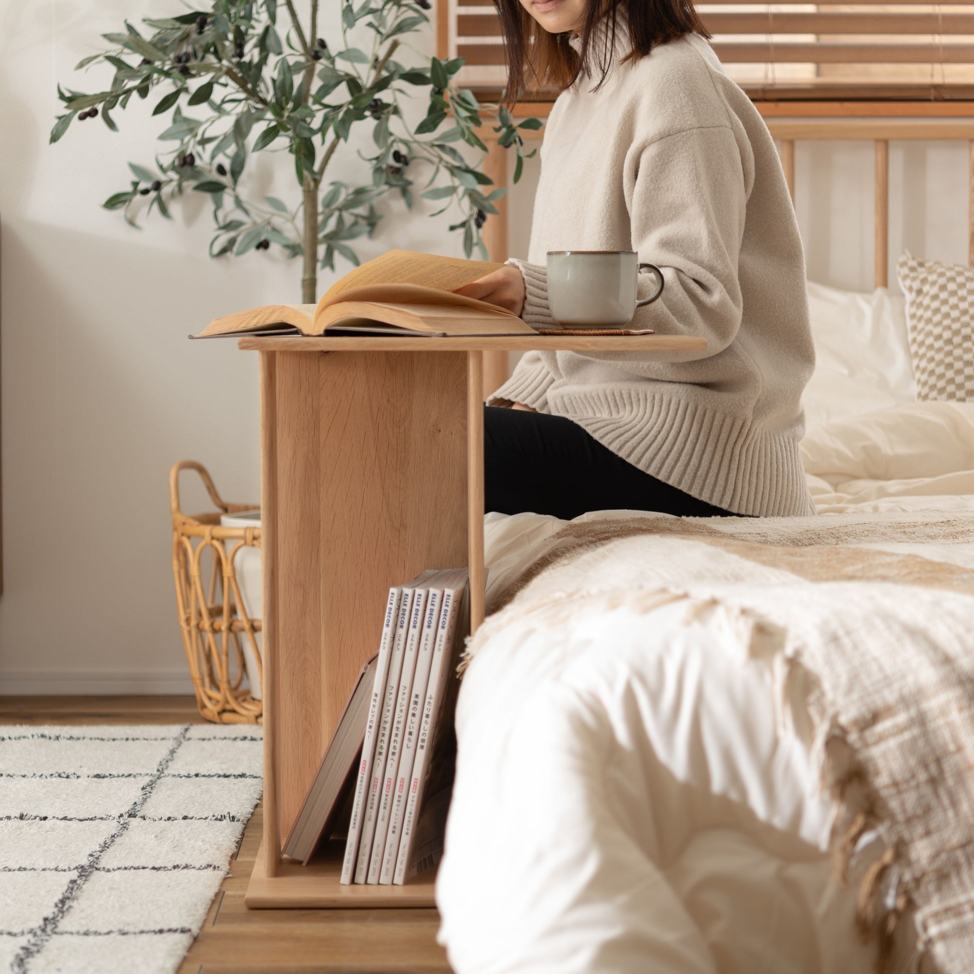 ラック付きオークサイドテーブルをベッド横に置き、お茶と本を読んでいる様子