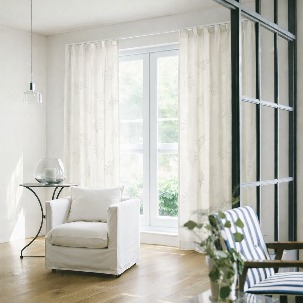 ベージュの繊細なリーフ柄の刺繍が目を引くやさしい表情のレースカーテンが窓にかかったリビング