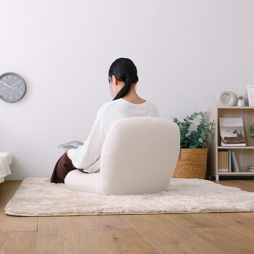 アイボリーのブークレ座椅子に腰掛けて雑誌を読んでいる様子